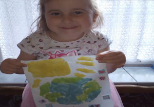 dziewczynka pokazuje swoją pracę wykonaną farbami rosnącymi na temat "dzień Ziemi": planeta, słońce